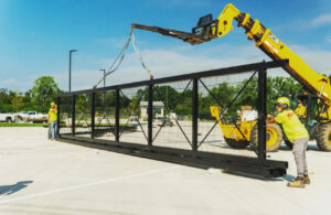 Workers installing a large black metal fence section with heavy machinery for Northway Fence in Menomonee Falls, WI.