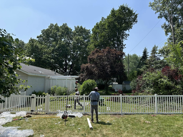 Workers from T & A Fencing installing a new white picket-style fence in a spacious backyard in Warren, MI.