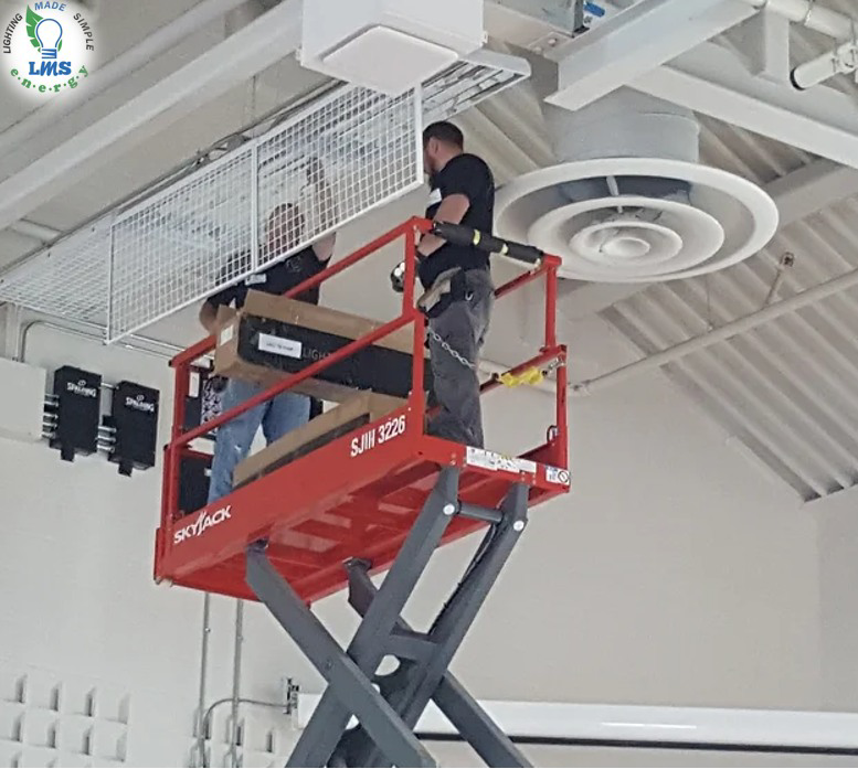 Workers from LMS Energy installing new overhead lighting fixtures from a scissor lift in a commercial building in Milwaukee, WI.
