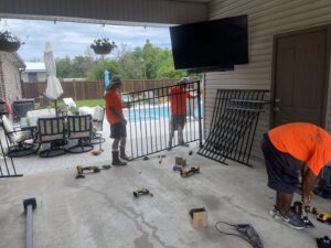 Workers from Southern Fencing, LLC installing black metal fence panels around a swimming pool in Houma, LA.