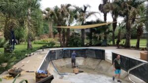 Two workers installing a new liner in an empty pool, with equipment around, demonstrating service by Brian's Pool Service in Baton Rouge, LA.