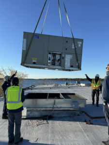 Workers guiding a large rooftop HVAC unit into place during an installation by Air Masters HVAC Services of New England, Inc. in Fall River, MA.