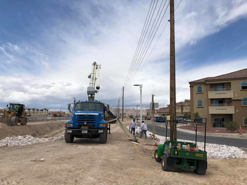 Workers installing a utility pole with a crane truck on a construction site for Desert Clark County Lighting in Las Vegas, NV.