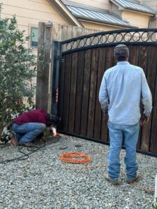 Two workers installing and welding a wooden and metal gate, a service by HDR Systems Gate, Fence & Garage doors in Plano, TX