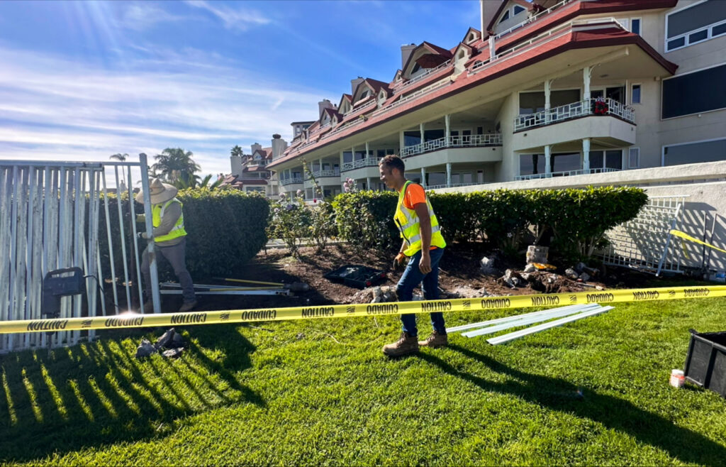 Two workers installing a white metal fence with caution tape, a project by San Diego Fencing Contractor A's Pro Build Fencing in San Diego, CA.