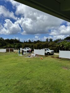 Workers installing a white vinyl fence in a large grassy area for Upright Fencing Hawaii LLC in Kapolei, HI.