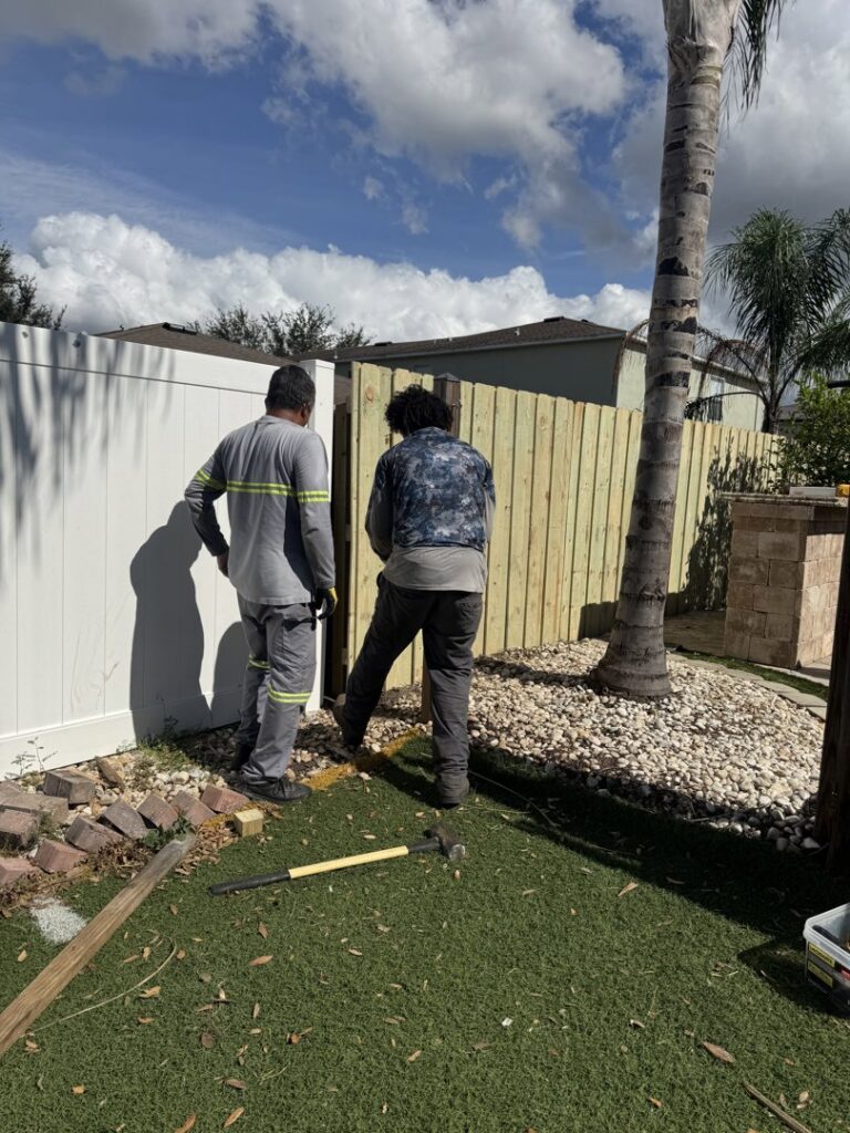 Two workers installing a new wood fence section next to a white vinyl fence for Santis Fence & Home Service in Tampa Heights, FL