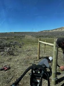 Workers installing a wood post and wire fence in a rural area for Tomahawk Fencing in Riverton, WY.