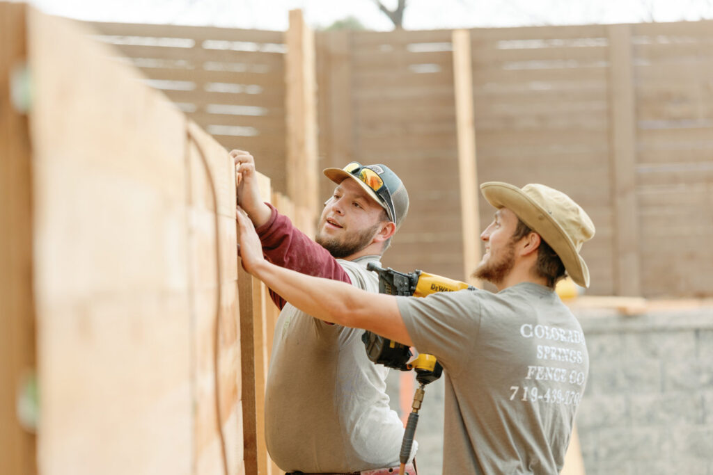 Two workers installing wooden fence panels, showcasing the work of Colorado Springs Fence Company in Colorado Springs, CO.