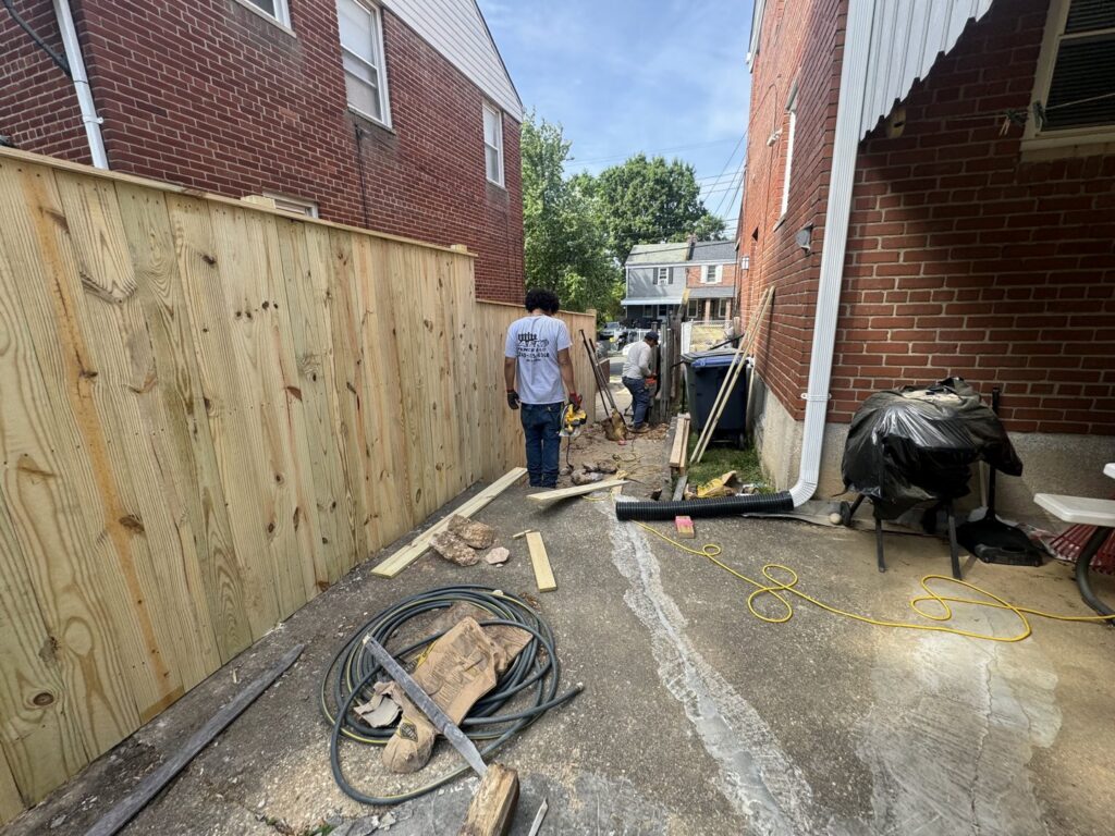 Workers installing a wooden privacy fence in a narrow alleyway between two brick houses for AFK FENCE LLC in Waldorf, MD.