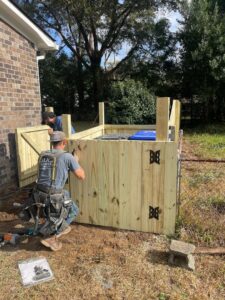 Two workers installing a wooden privacy fence enclosure for trash cans by Stono Fencing & Exteriors in Johns Island, SC