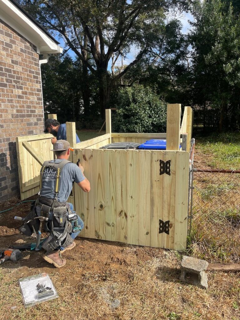 Two workers installing a wooden privacy fence enclosure for trash cans by Stono Fencing & Exteriors in Johns Island, SC