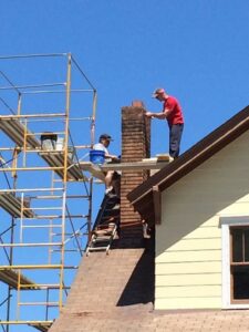 Two workers on scaffolding performing masonry repair work on a residential chimney for The Chimney Doctor in Louisville, KY.