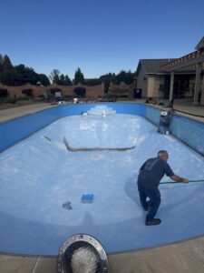 Two workers painting the interior of an empty inground pool, preparing for a new liner installation by Westside Pools in Owensboro, KY.