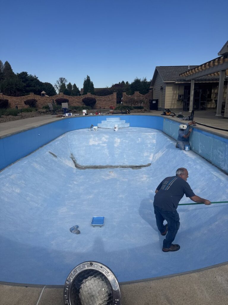 Two workers painting the interior of an empty inground pool, preparing for a new liner installation by Westside Pools in Owensboro, KY.