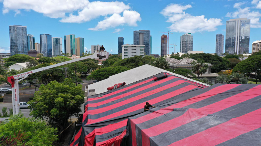 Workers on a roof tarping a building for fumigation with a boom lift by Kama'aina Termite and Pest Control in Honolulu, HI.