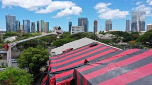 Workers on a roof tarping a building for fumigation with a boom lift by Kama'aina Termite and Pest Control in Honolulu, HI.