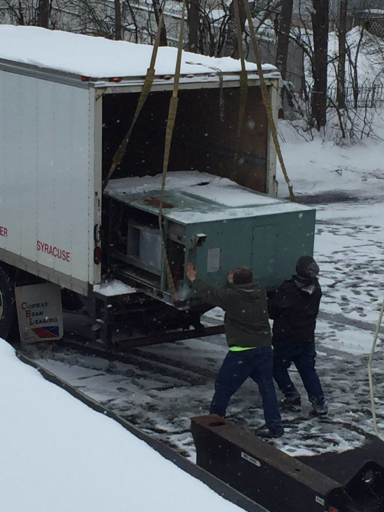 Two workers carefully unloading a large HVAC unit from a truck in snowy conditions, handled by Spencer Heating & Air Conditioning in Norcross, GA.