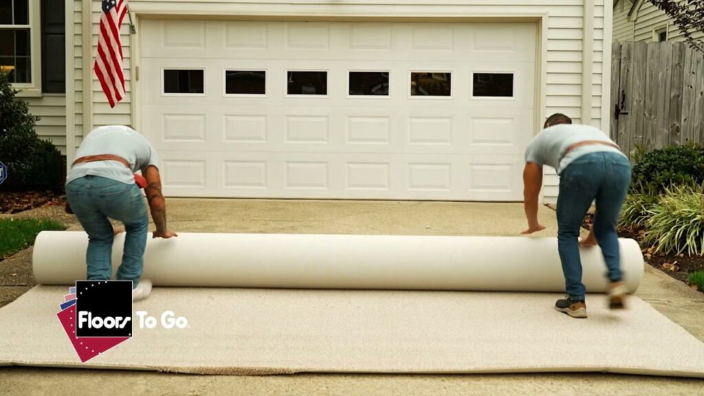 Two workers from Floors To Go unrolling a large carpet roll on a driveway for installation at a home in Virginia Beach, VA.
