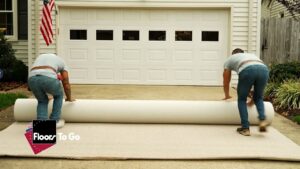 Two workers from Floors To Go unrolling a large carpet roll on a driveway for installation at a home in Virginia Beach, VA.
