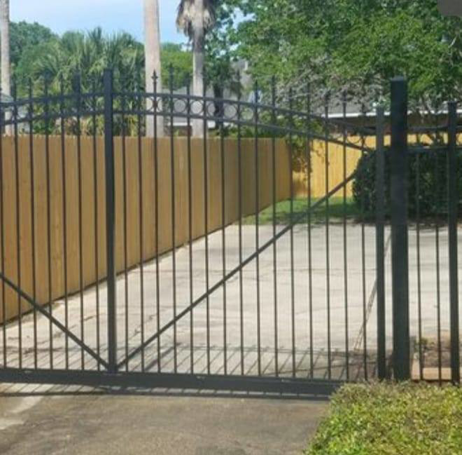 A black wrought iron gate installed in front of a wooden fence by Weber Deck & Fence in Baton Rouge, LA.
