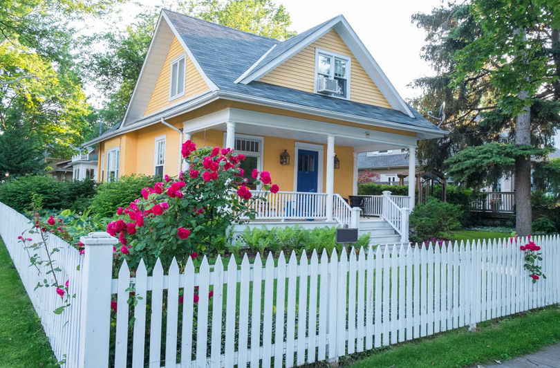 A charming yellow house with a beautiful white picket fence and vibrant red roses by New Bedford Fence in New Bedford, MA.