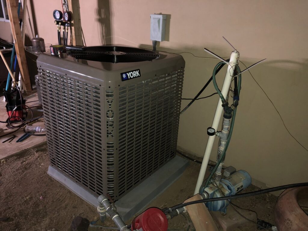 An outdoor York AC condenser unit undergoing maintenance or installation with tools and pipes by Hellerud Air in Peoria, AZ.