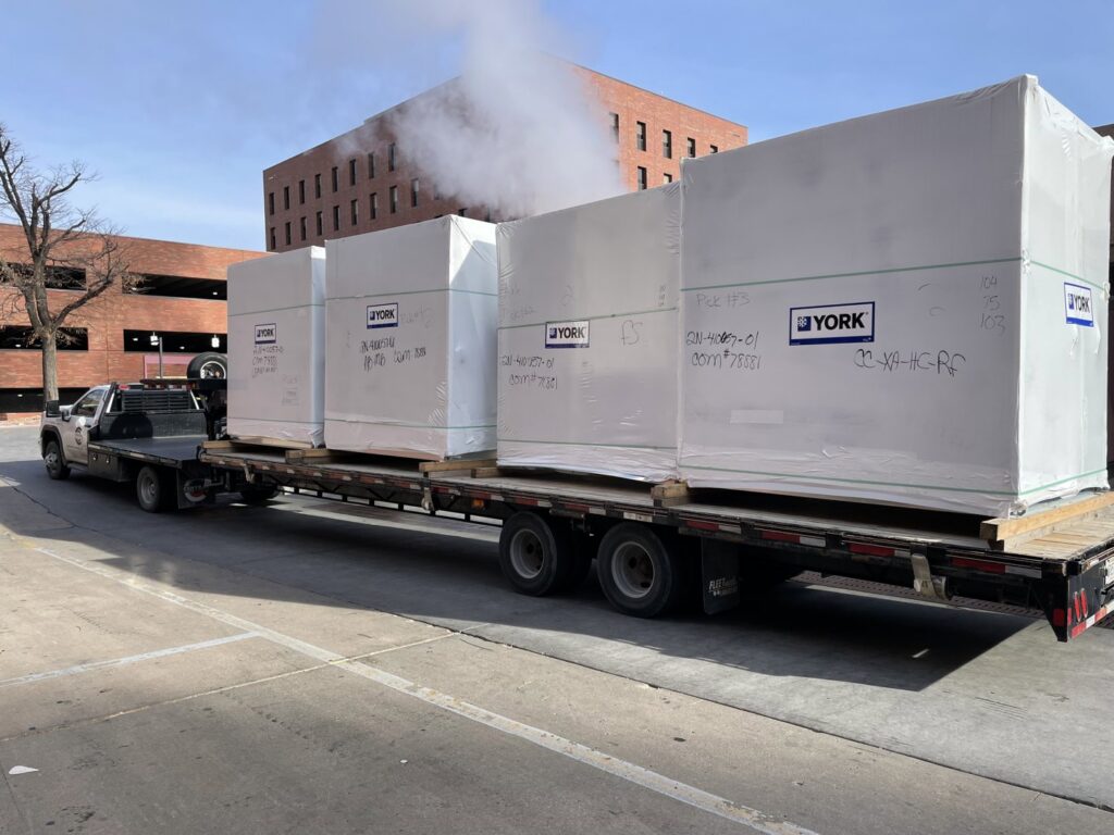 A flatbed truck delivering large, wrapped YORK HVAC units for a project by Central Consolidated in Wichita, KS