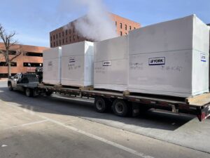A flatbed truck delivering large, wrapped YORK HVAC units for a project by Central Consolidated in Wichita, KS