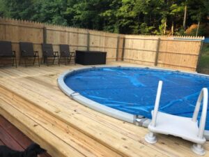 An above-ground oval pool with a blue cover and wooden deck installed by Pool Queen in Fairmont, WV.