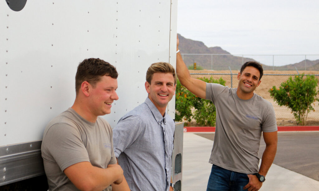 Three friendly Academy Movers team members smiling while leaning against a moving truck in Gilbert, AZ.
