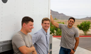 Three friendly Academy Movers team members smiling while leaning against a moving truck in Gilbert, AZ.