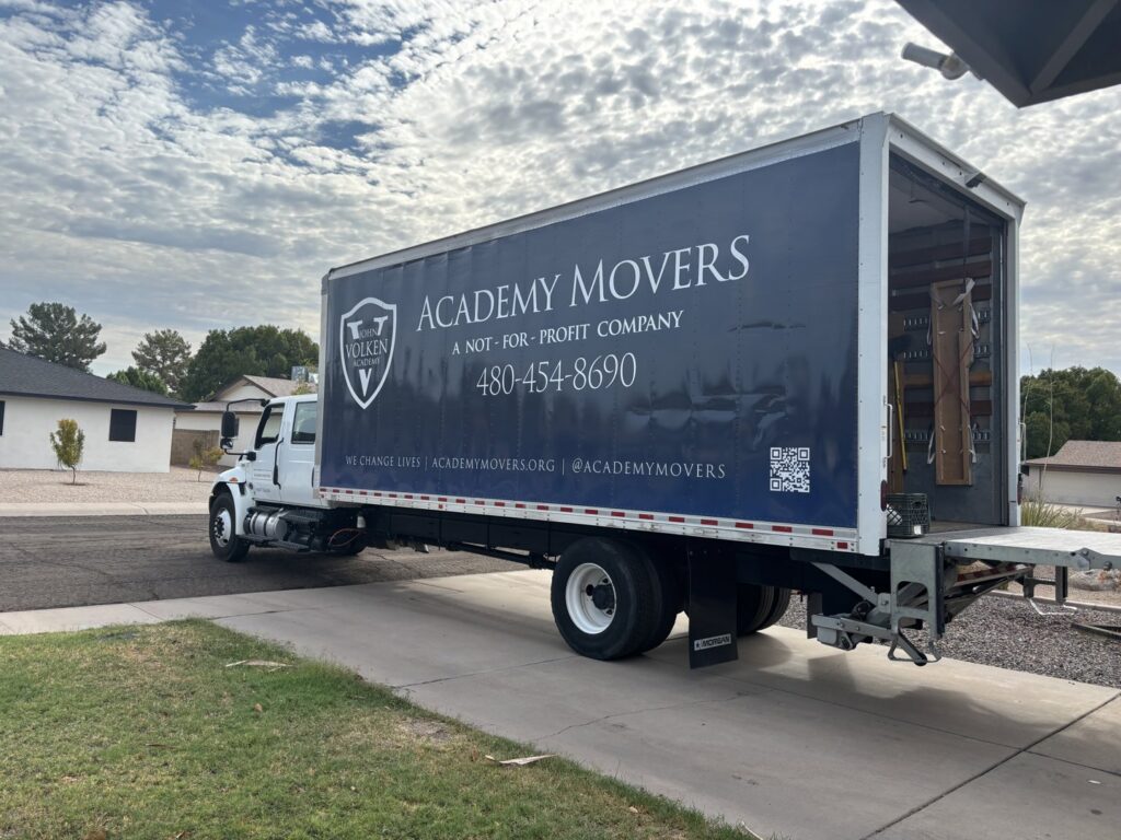 An Academy Movers branded moving truck with its ramp down, parked in a residential driveway in Gilbert, AZ, ready for a job.