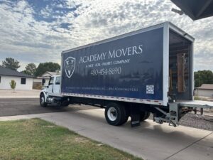 An Academy Movers branded moving truck with its ramp down, parked in a residential driveway in Gilbert, AZ, ready for a job.