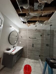 Active water leaking from a damaged ceiling into a bucket in a bathroom, indicating severe water damage, handled by Level Creek Property Restoration in Buford, GA.