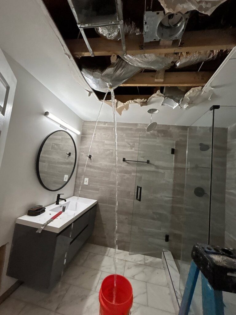 Active water leaking from a damaged ceiling into a bucket in a bathroom, indicating severe water damage, handled by Level Creek Property Restoration in Buford, GA.