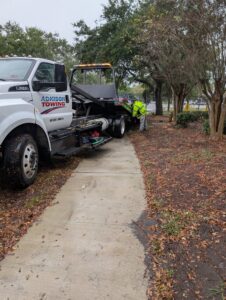 An Adkison Towing employee loading a green car onto a flatbed tow truck for transport in Jacksonville, FL.