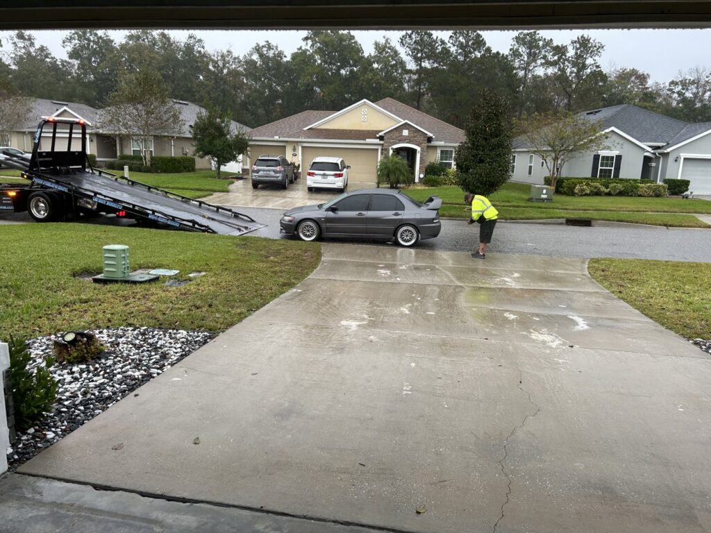 An Adkison Towing employee preparing a grey car for transport on a flatbed truck in Jacksonville, FL.