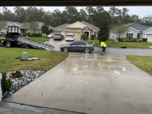An Adkison Towing employee preparing a grey car for transport on a flatbed truck in Jacksonville, FL.