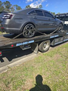 Adkison Towing flatbed truck transporting a grey sedan on a sunny day in Jacksonville, FL.