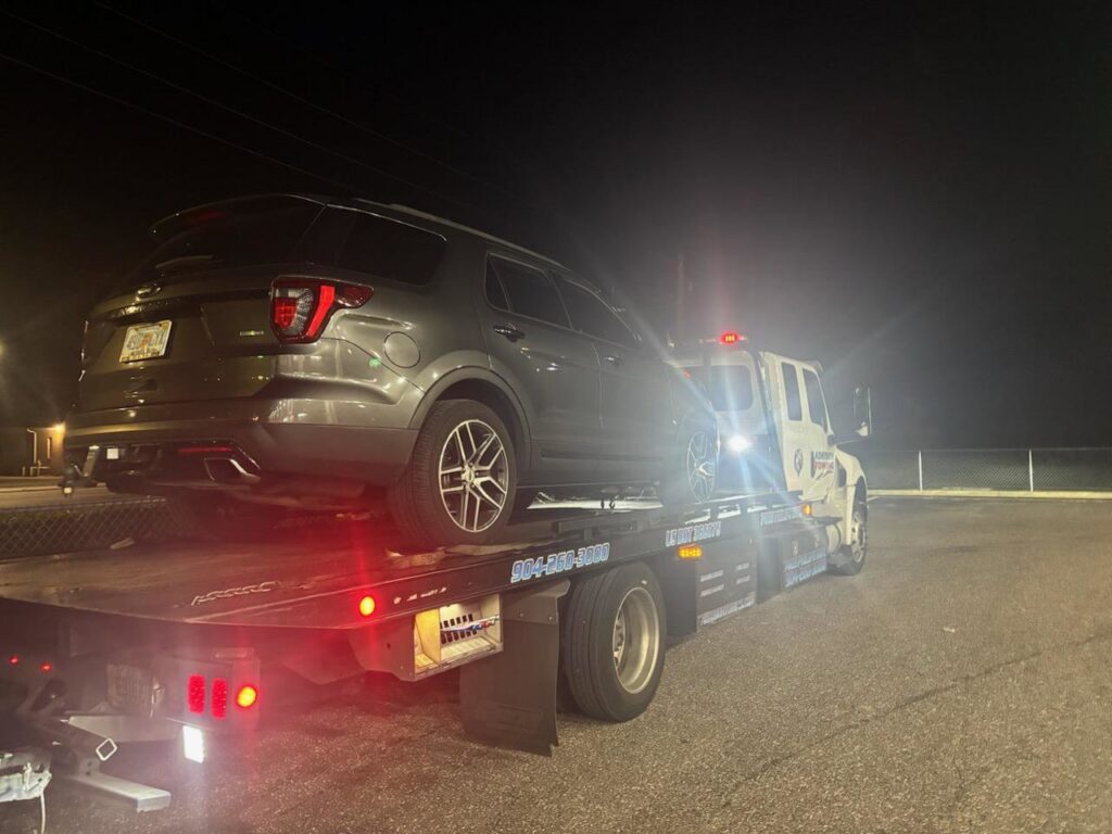 Adkison Towing flatbed truck transporting a grey SUV at night in Jacksonville, FL.