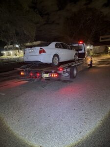 Adkison Towing flatbed truck transporting a white sedan at night in Jacksonville, FL.