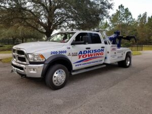 A white Adkison Towing flatbed truck parked on a paved surface, ready for transport in Jacksonville, FL.