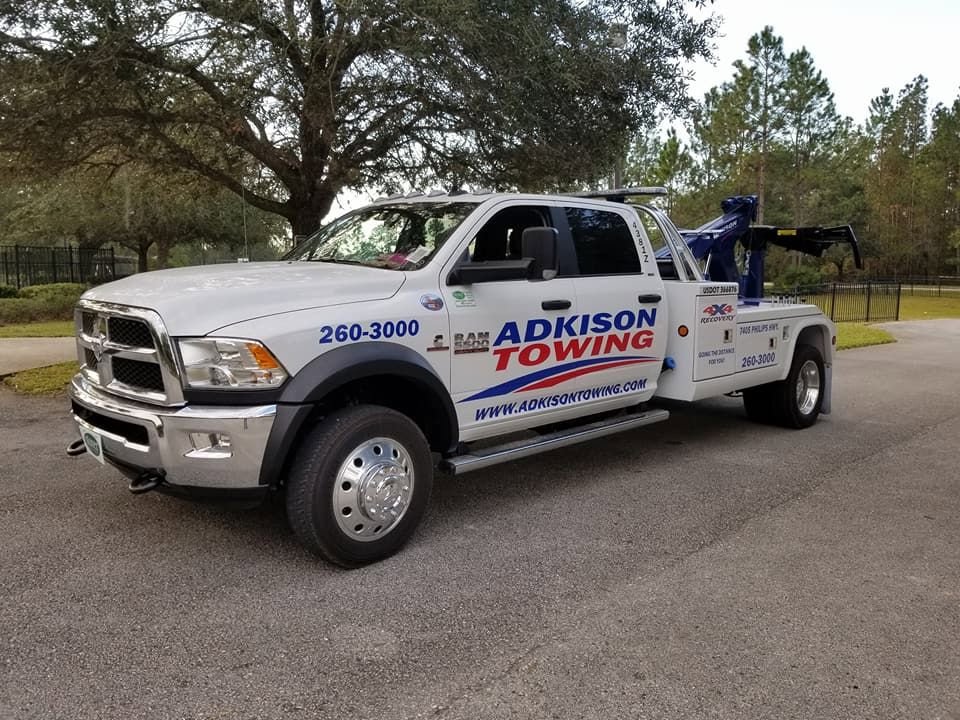 A white Adkison Towing flatbed truck parked on a paved surface, ready for transport in Jacksonville, FL.