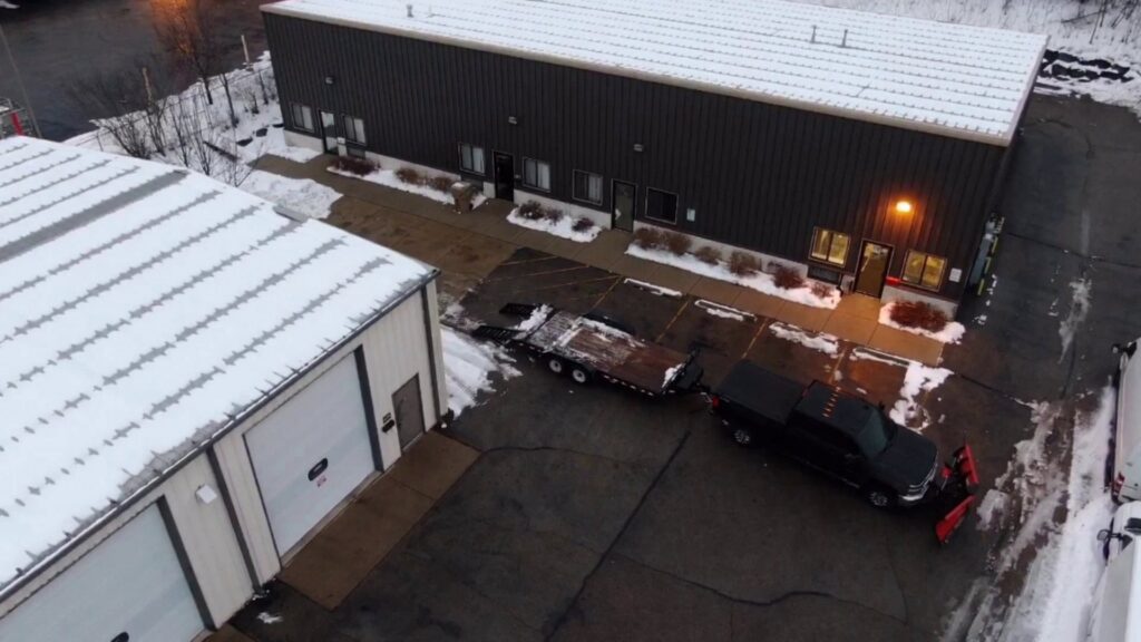 An aerial view of a commercial property with a truck and snow plow performing snow removal by Haynes Snow Removal & Lawn Maintenance in Madison, WI.