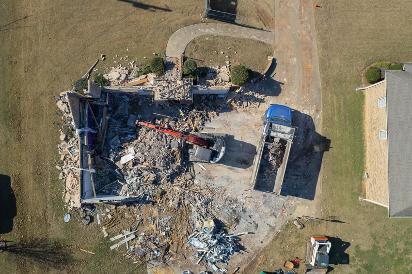 Aerial view of a residential house being demolished by an excavator and dump truck at a Nuckles Services job site in Birmingham, AL