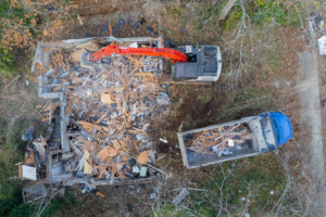 Aerial view of an excavator loading demolition debris from a residential property into a dump truck for Nuckles Services in Birmingham, AL