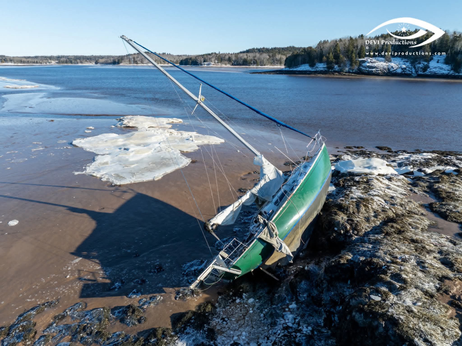 Aerial view of a beached sailboat on a snowy shore, requiring salvage services from Downeast Marine Towing, LLC in Eastport, ME.