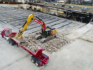 An aerial view of an excavator loading demolition debris into a truck for DeCarlo Demolition Company in Des Moines, IA.