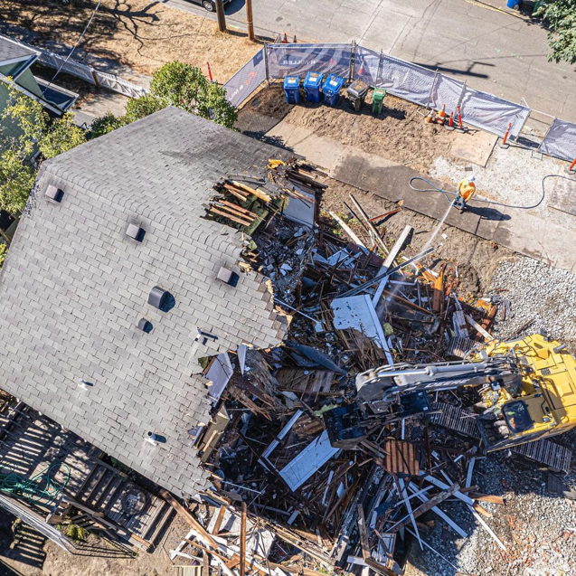 Aerial view of a house being demolished by an excavator, showing active demolition work by Rainstate Earthworks in Auburn, WA.